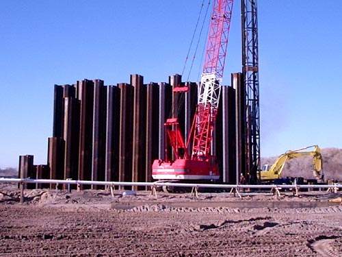 Looking southerly from the north cofferdam area riverbed, the photo shows a crane and diesel impact hammer positioning upstream sheet piles.